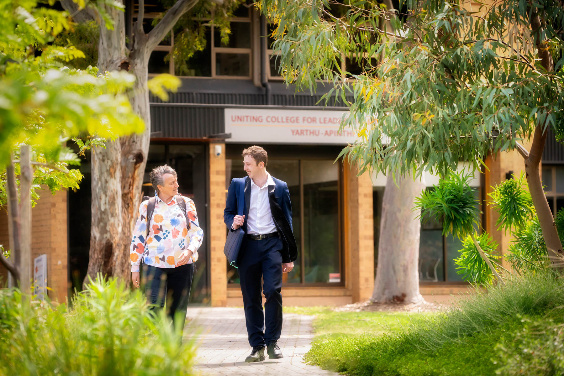 Two students walk outside Uniting College for Leadership and Theology with gumtrees bordering the path.