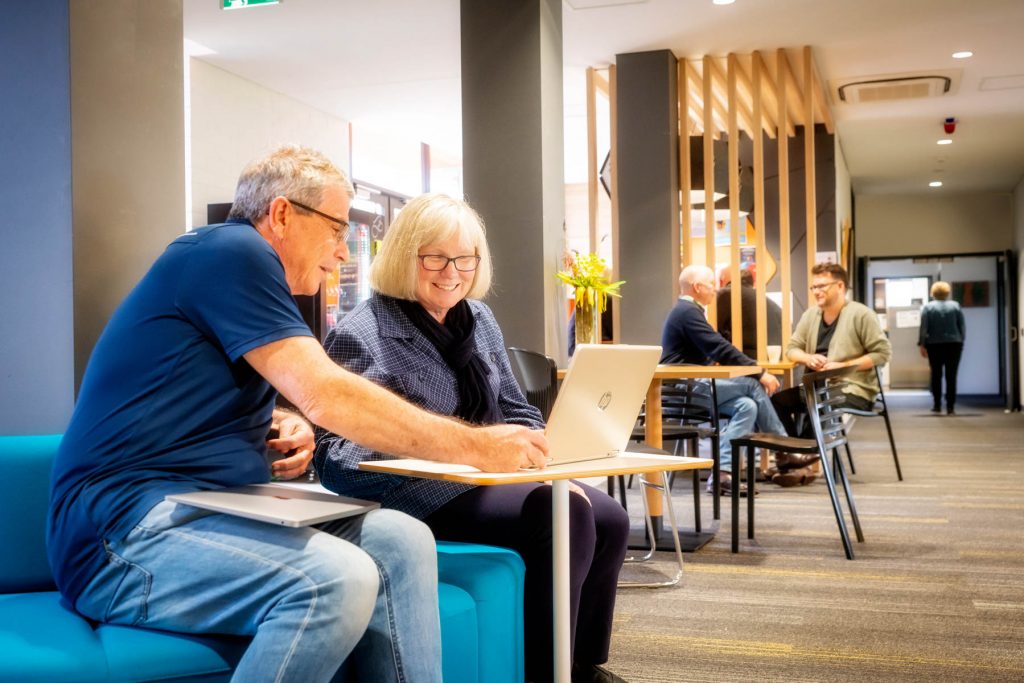 A man in a blue shirt shows a Uniting College for Leadership and Theology student something on her laptop.