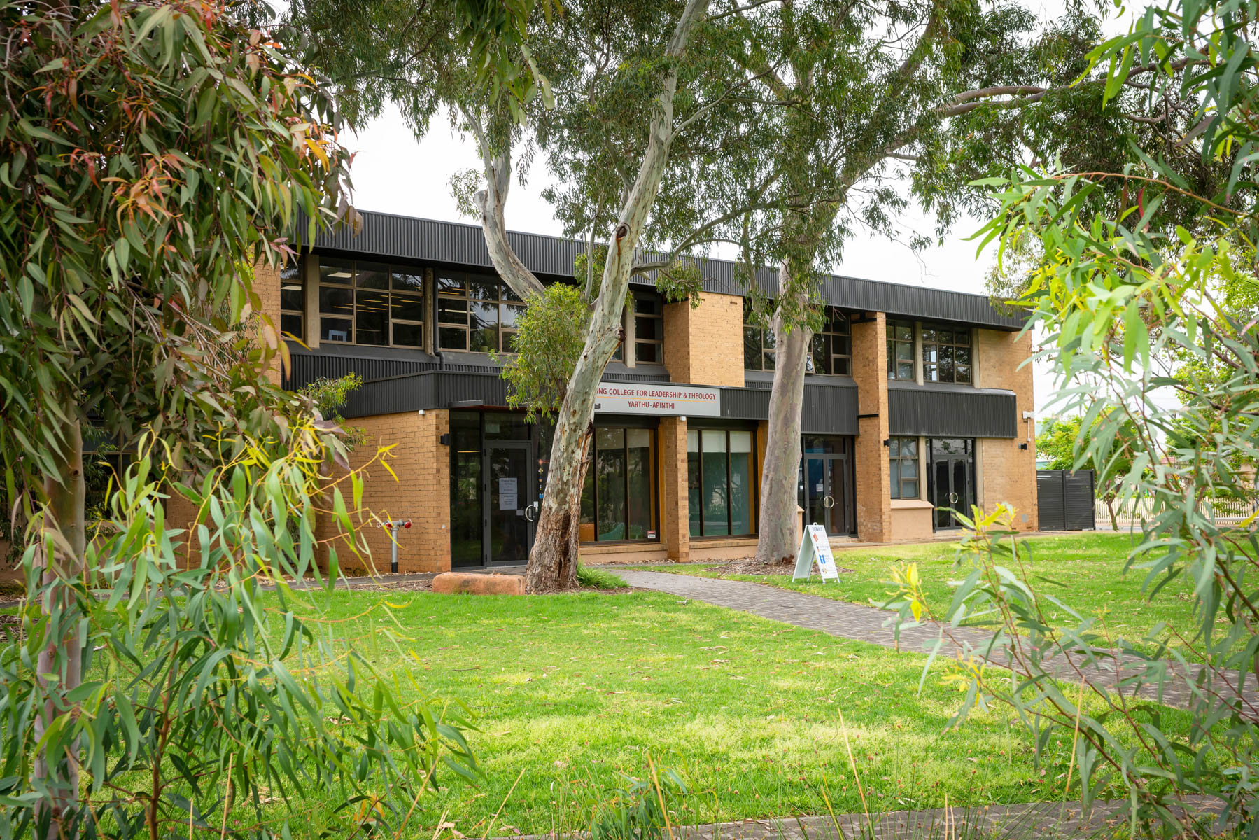The exterior of Uniting College for Leadership and Theology, surrounded by green grass and gum trees.