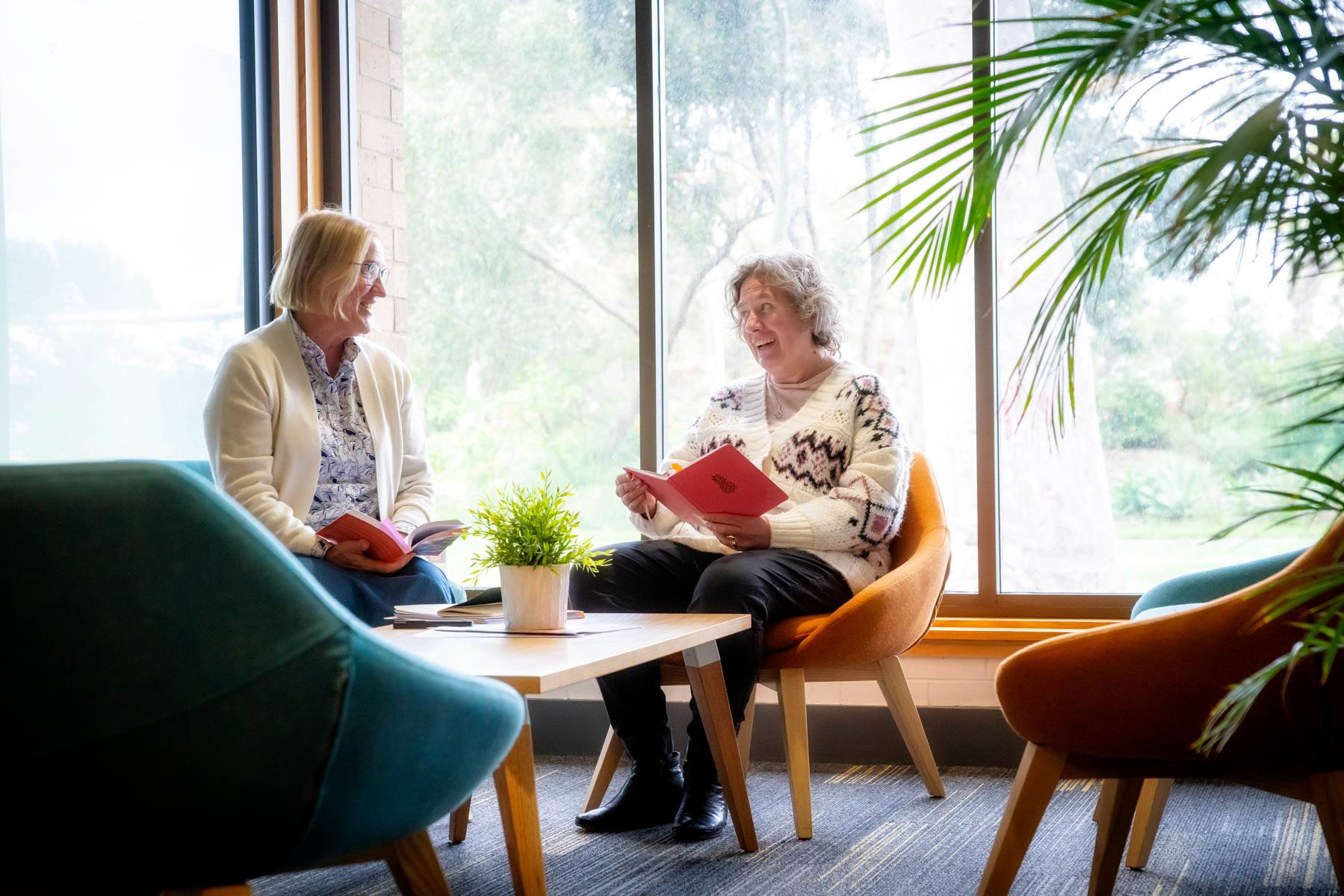 Two Uniting College for Leadership and Theology students sit around a table chatting with books open in their hands.