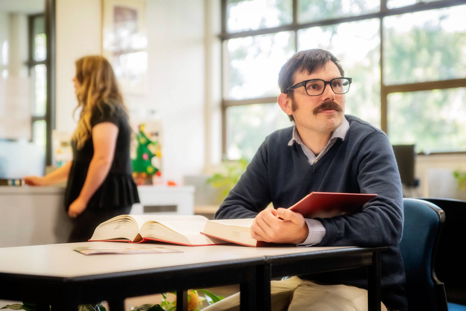 A student in black glasses from Uniting College for Leadership and Theology reads a red book at a library table