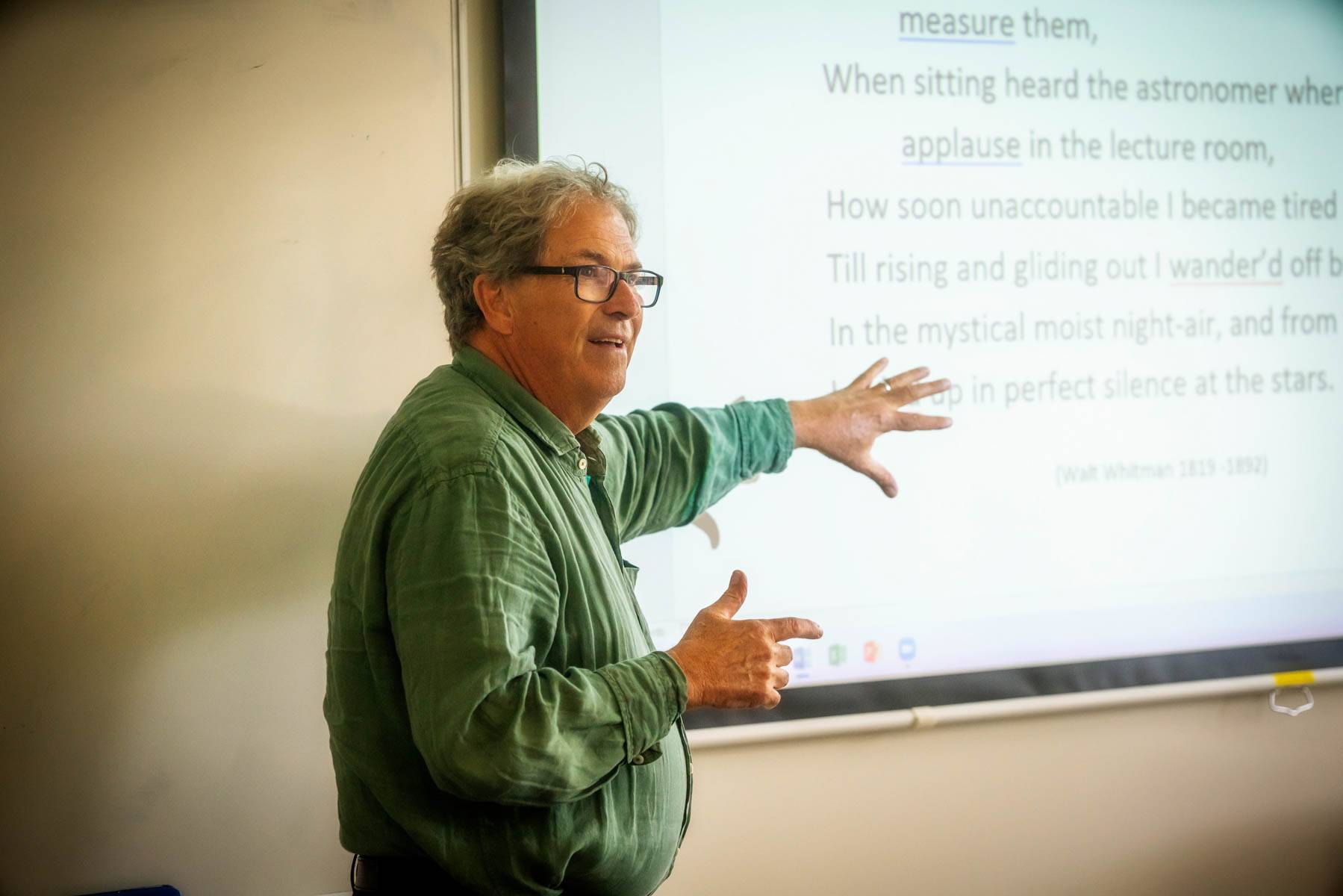 A lecturer in a green shirt presents some text projected on a screen