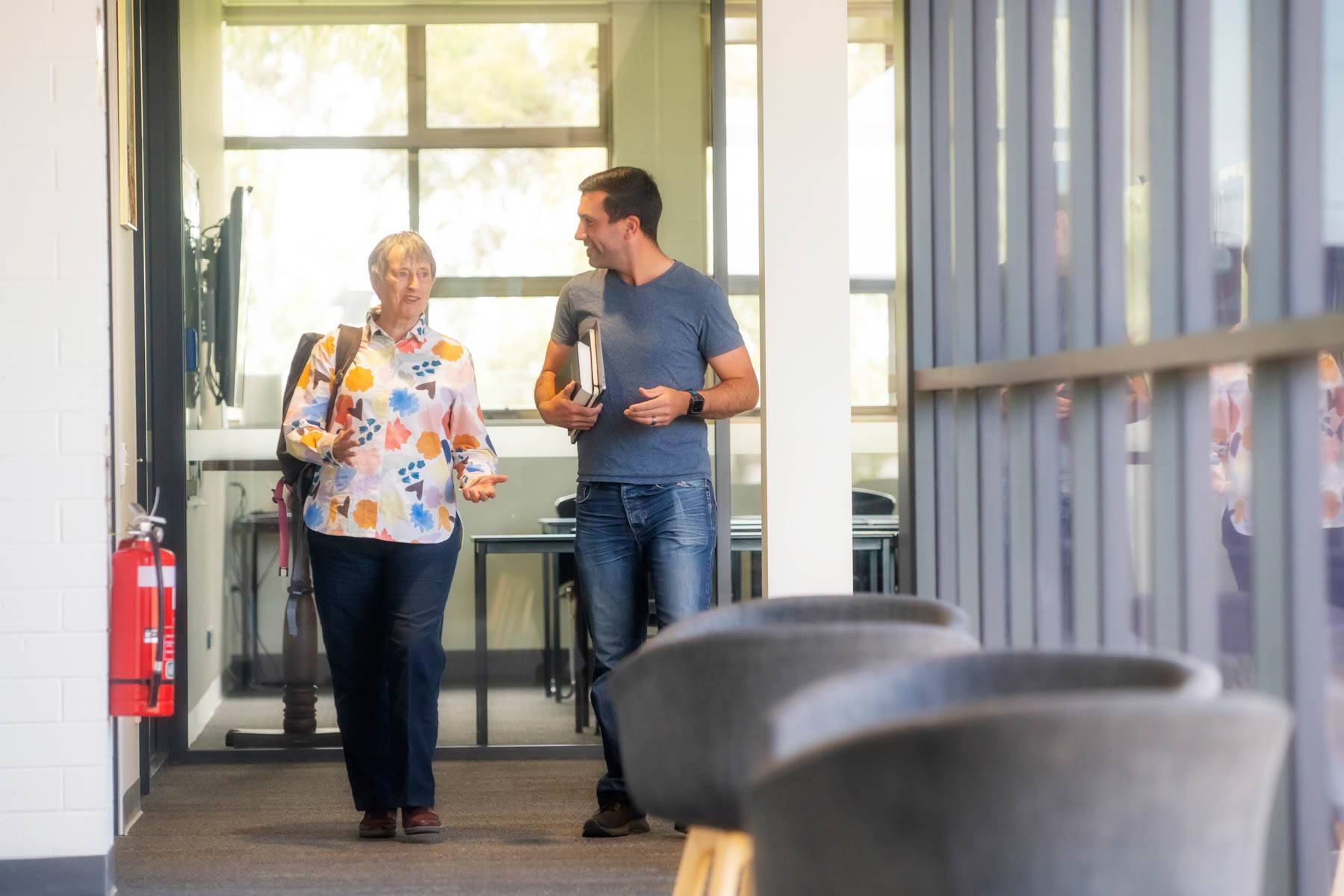 Uniting College for Leadership and Theology students walk down a campus hall carrying books and in conversation