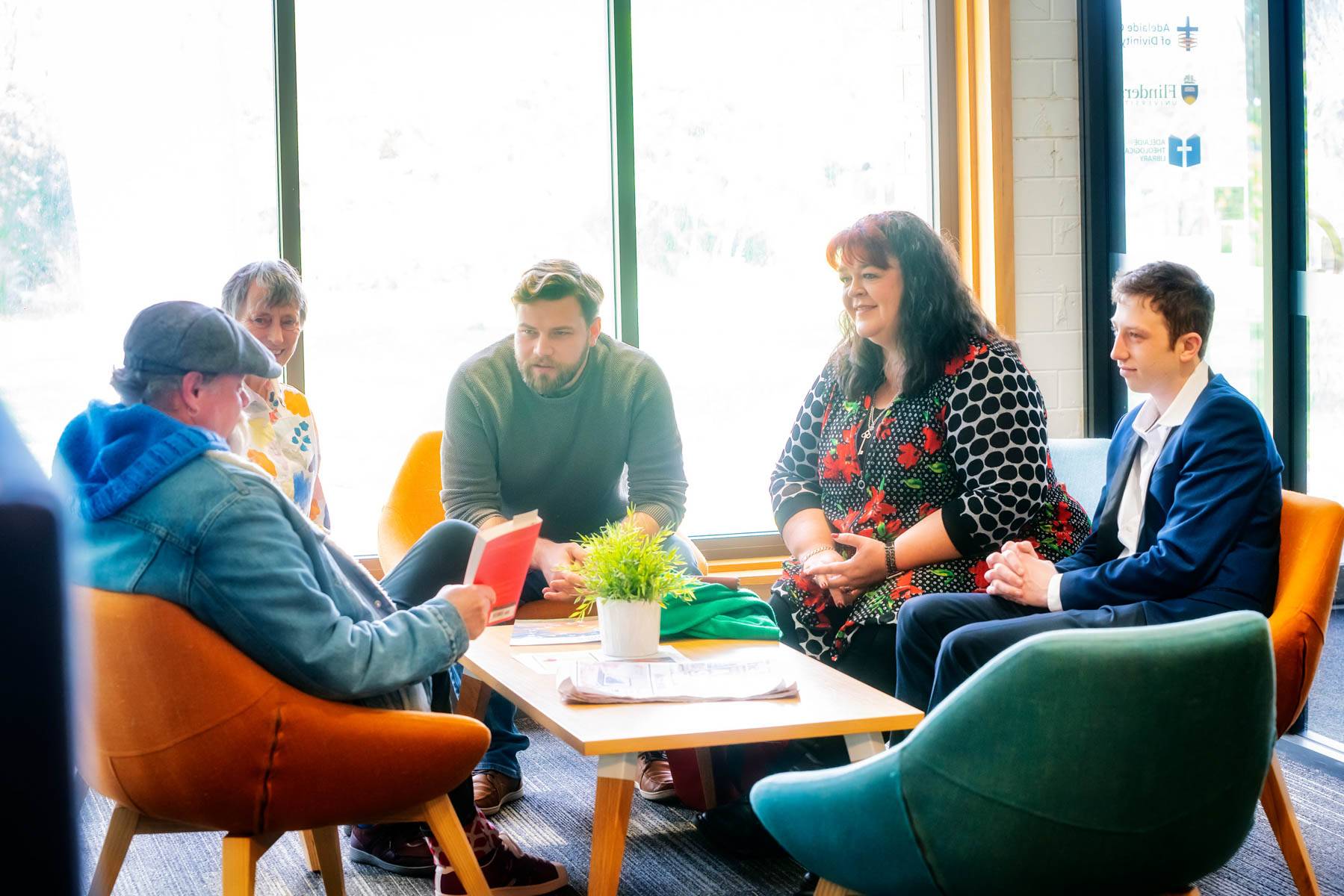 Several Uniting College for Leadership and Theology students sit around a table as one students shows them a book